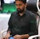 A person is seated in a chair, focused intently on something, with hands positioned on a gaming console or arcade controller. The setup appears to be indoors, with visible screens and lighting in the background, suggesting an electronic gaming environment.
